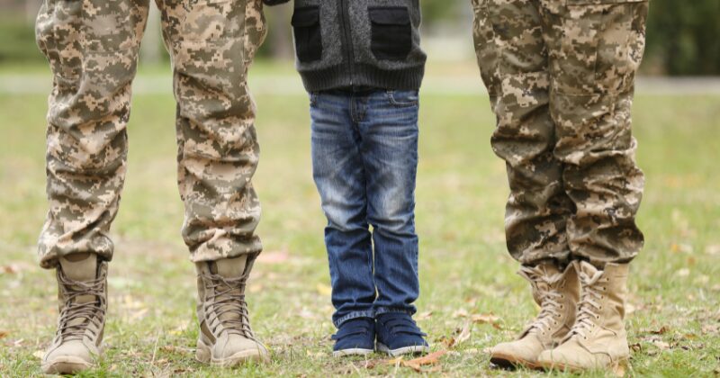 Legs of male and female military service members with child between them on grass, representing dual income home buying power.